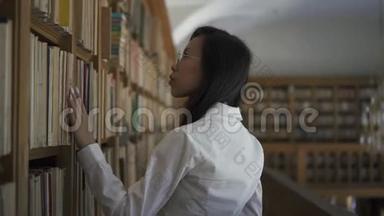 年轻的亚洲女研究员正在寻找书架上的书
